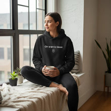 Charger l'image dans la galerie, Femme portant un hoodie noir Impressions Gaspésie avec inscription On s'en k lisse, assise près d'une fenêtre.