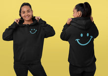 Charger l'image dans la galerie, Femme portant le hoodie noir Impressions Gaspésie avec un motif sourire bleu sur la poitrine et dans le dos