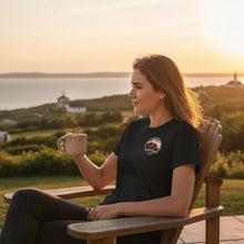 Charger l'image dans la galerie, Femme portant un t-shirt noir Impressions Gaspésie avec logo La belle Gaspésie, assise avec une tasse au coucher