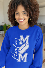 Charger l'image dans la galerie, Femme souriante portant un chandail bleu Impressions Gaspésie avec inscription Hockey Mom et motif de rondelle
