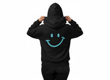 Charger l'image dans la galerie, Vue arrière du hoodie noir Impressions Gaspésie avec un grand motif de sourire bleu clair sur le dos
