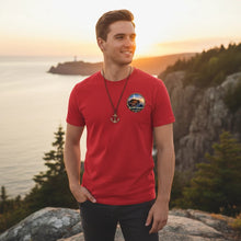Charger l'image dans la galerie, Homme portant un t-shirt rouge Impressions Gaspésie avec logo circulaire, devant un paysage côtier au coucher du soleil
